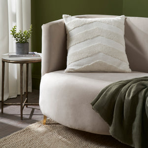 Chiara Indoor Pillow on a beige curved sofa with a green wall background