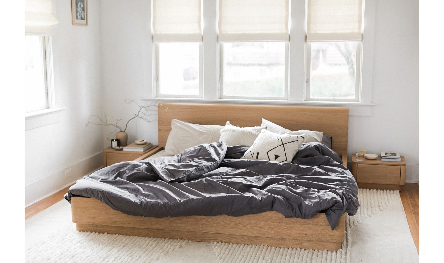Bedroom with a wooden bed frame and gray bedding, natural light coming through windows.