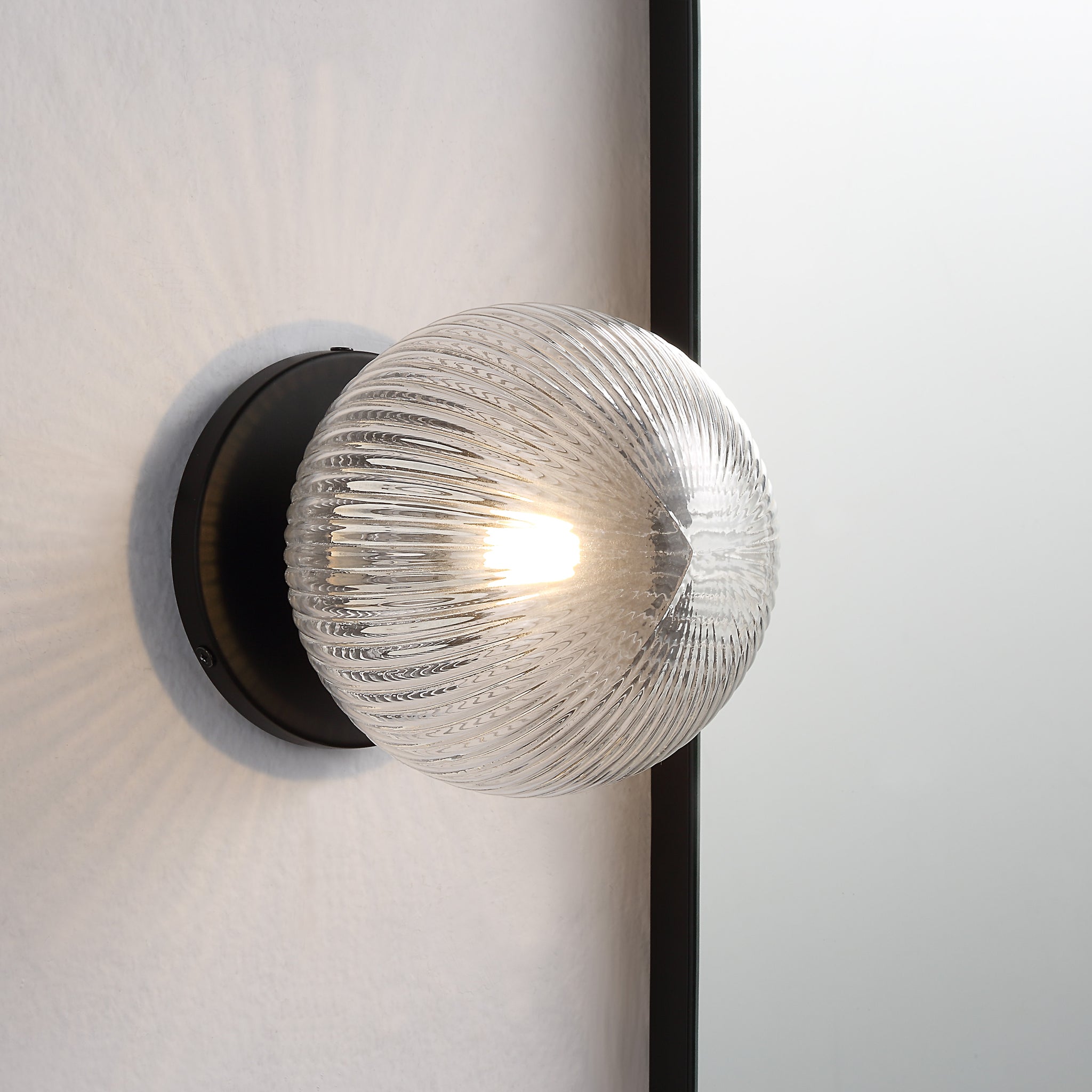 Brian Wall Sconce illuminated, showing the clear ribbed glass globe mounted on a wall.