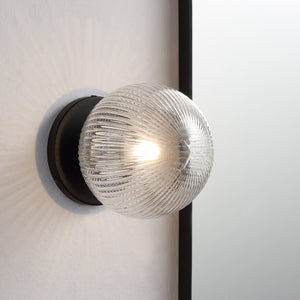 Brian Wall Sconce illuminated, showing the clear ribbed glass globe mounted on a wall.