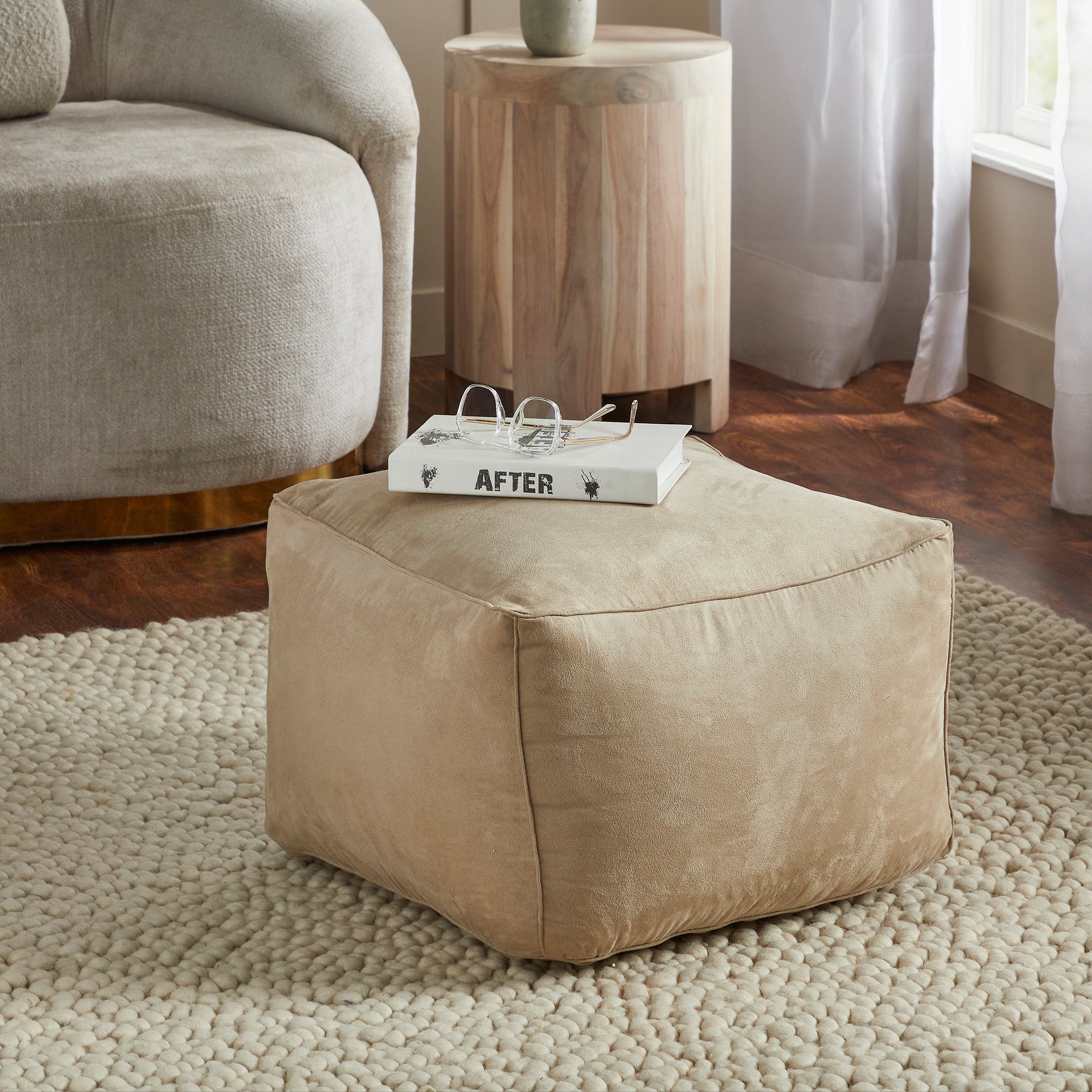 Bundle Pouf in beige, styled with a book and glasses on top, placed on a textured rug.