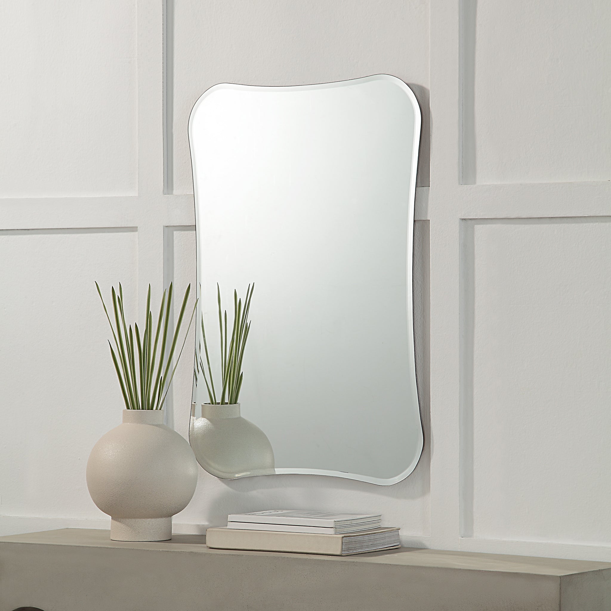 Kalmia Wall Mirror displayed above a modern vase and books on a shelf
